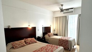 A hotel room with two beds, a ceiling fan, and a window with curtains. - Palermo Bridge (Buenos Aires)