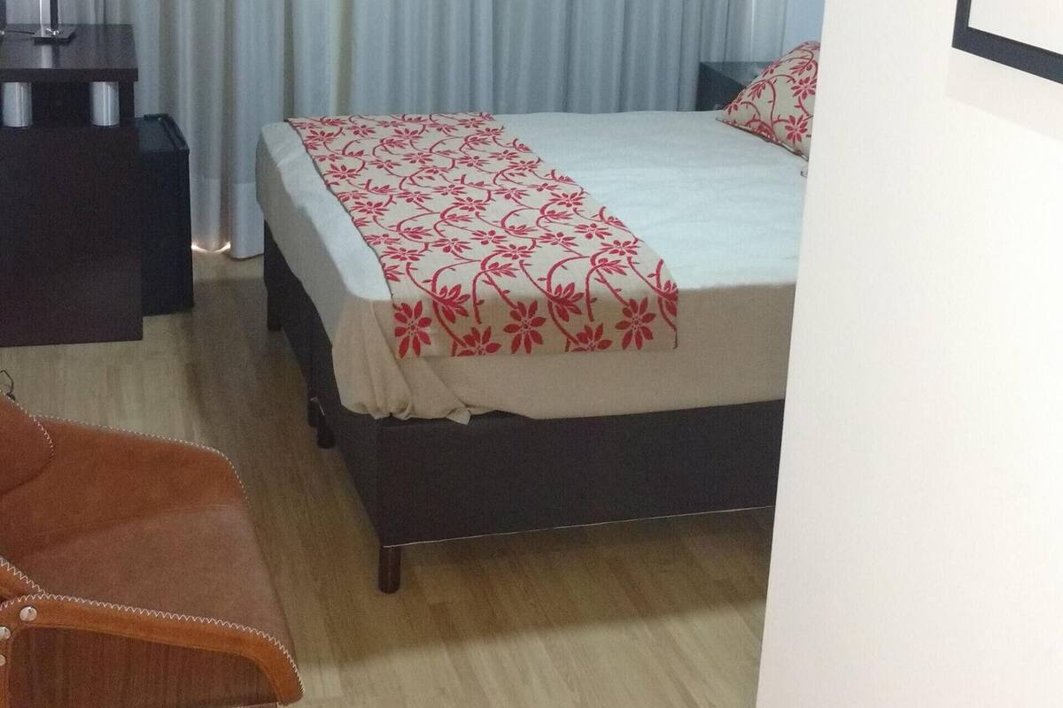 Habitación de hotel con cama, una silla, escritorio, ventilador de techo y ventana con cortinas.