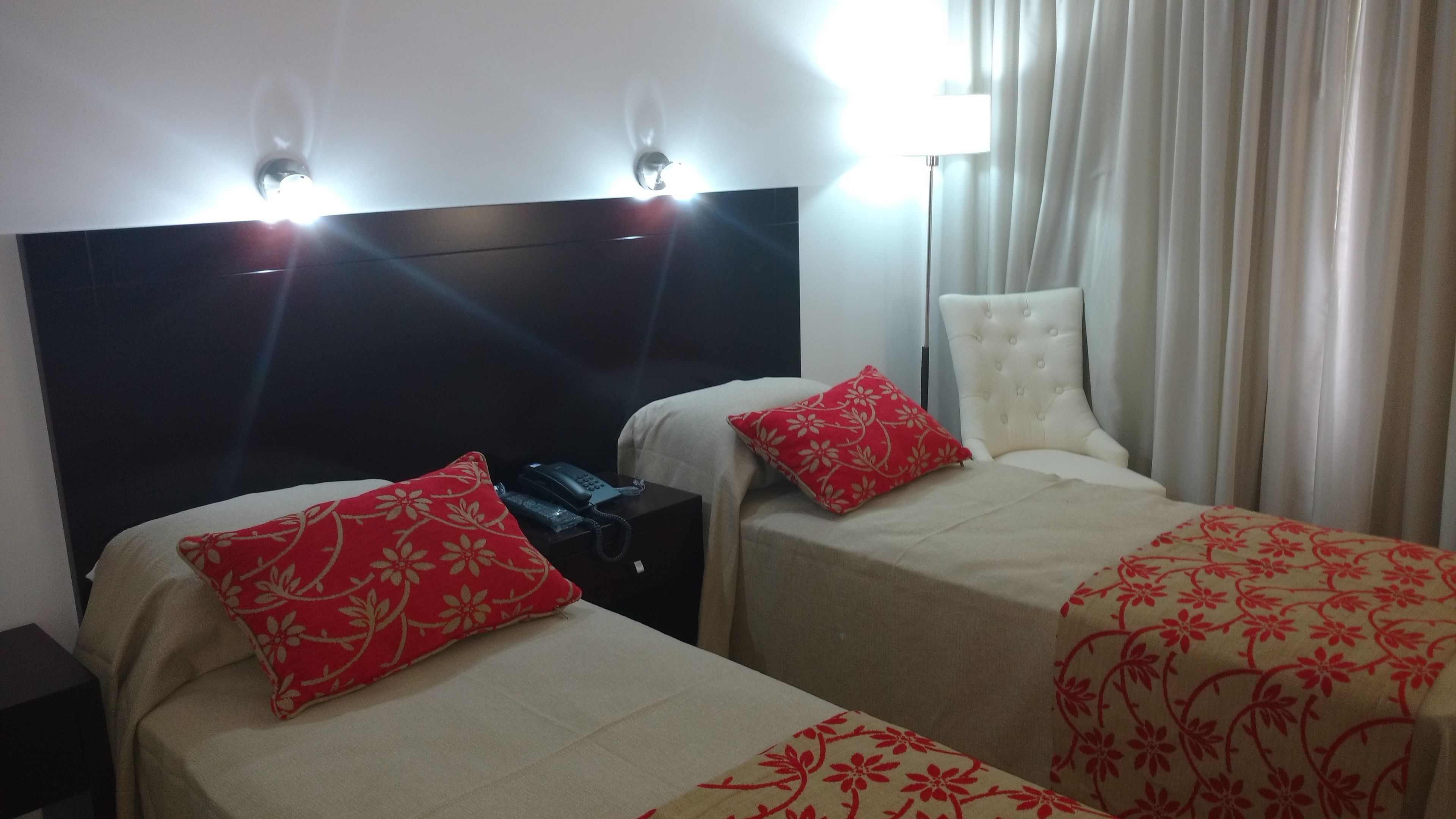 A hotel room with two beds, each with a red floral pillow and a white headboard. There is a nightstand with a telephone on it.