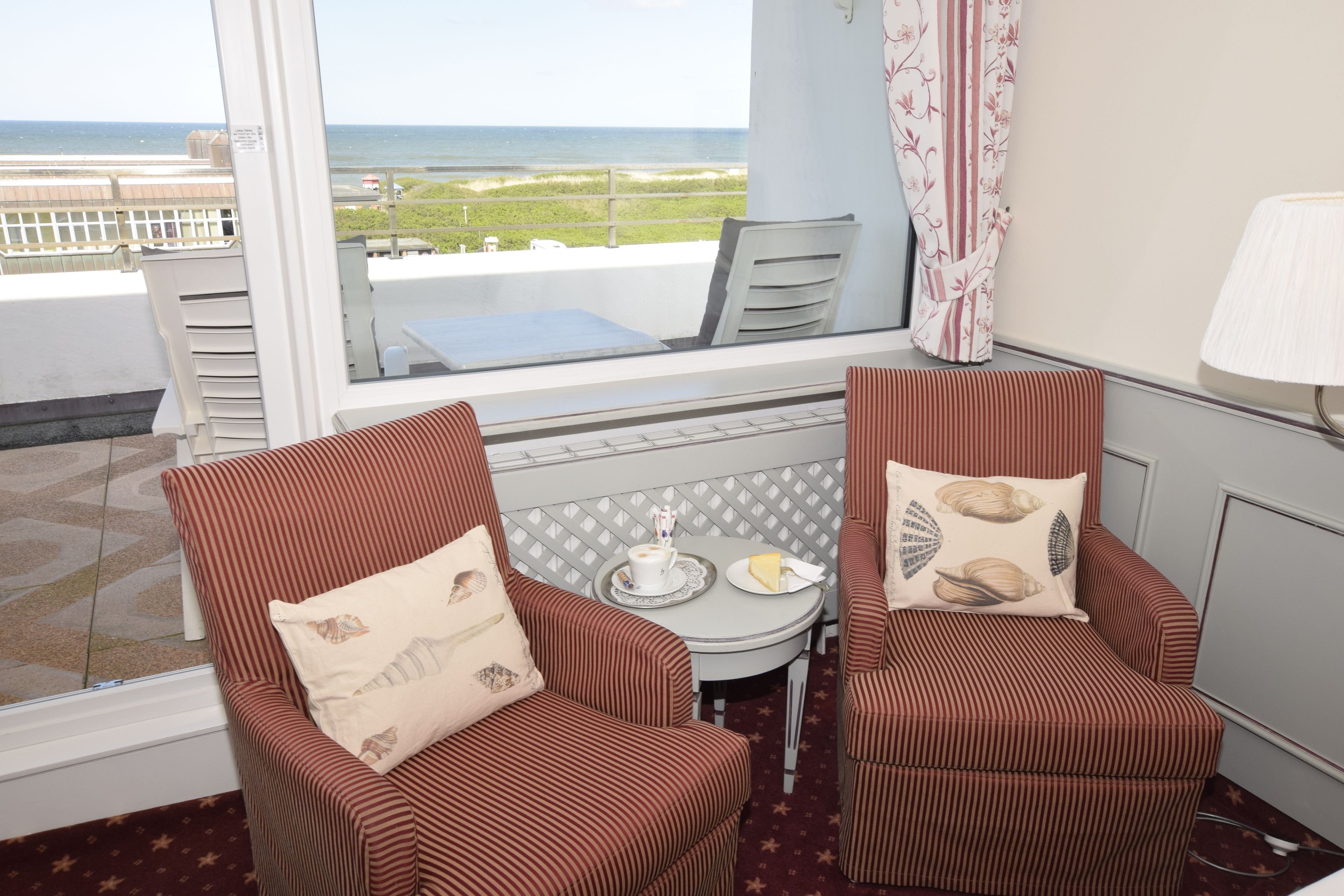 Un balcon avec deux chaises à rayures, une petite table avec une tasse et une assiette, et une vue sur la plage.