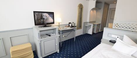 Habitación de hotel con cama, escritorio con televisor, espejo y un taburete pequeño.