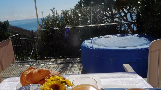 Una mesa con croissants, un vaso de jugo de naranja y una taza de café, frente a una vista panorámica del mar y árboles.