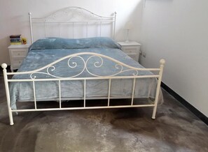 A white metal bed with a decorative headboard, a bedside table with a lamp, and a small stack of books. - La Casa dei Limoni (Genoa)