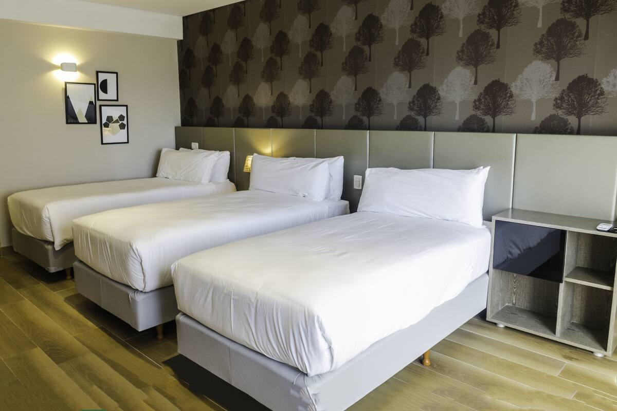 A hotel room with two single beds, a nightstand, and a wall with a tree pattern.