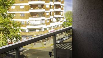 Un balcón con vistas a un edificio de varios pisos, un paso de peatones y coches aparcados.