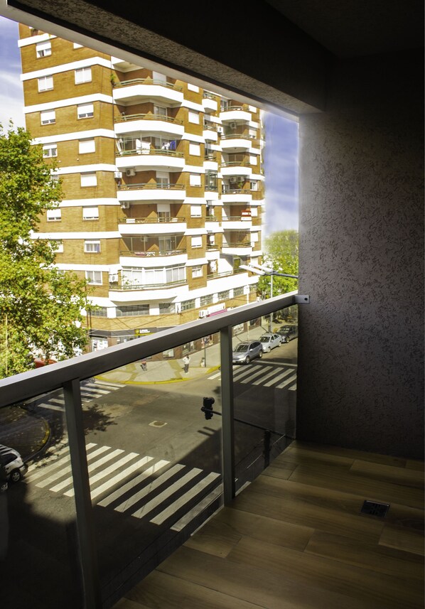 A balcony with a view of a multi-story building, a pedestrian crossing, and parked cars. - Avellaneda Aparts & Suites (Buenos Aires)