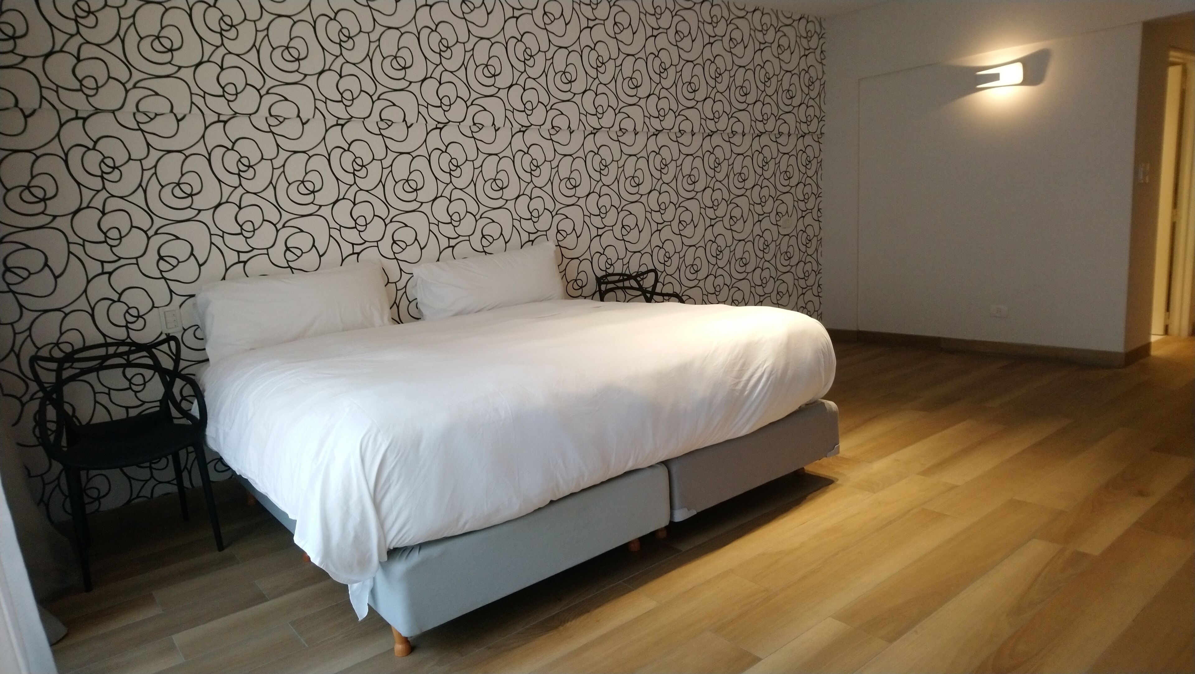 A bedroom with a bed, a chair, and a wall with a floral pattern.