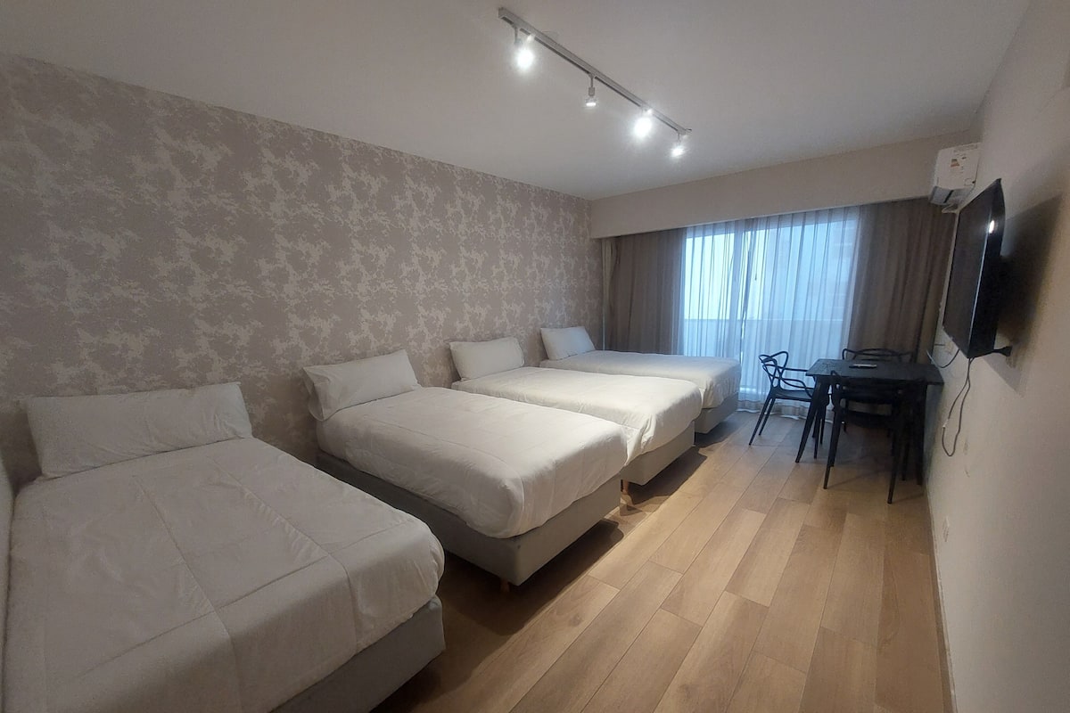 A hotel room with two beds, a desk, a chair, and a TV on the wall.