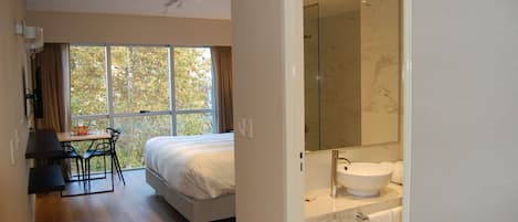A bedroom with a bed, a desk, and a window with curtains.