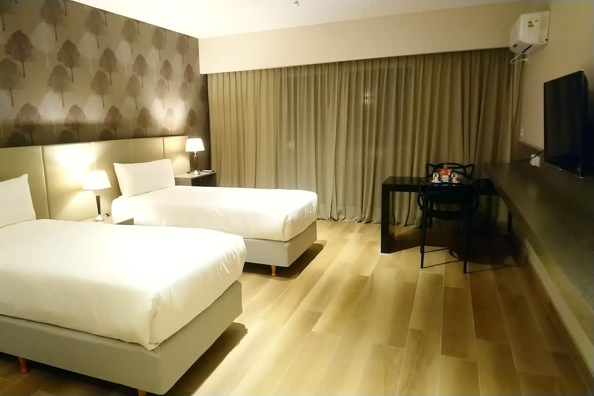 A hotel room with two beds, a desk, a chair, a TV, and a window with curtains.