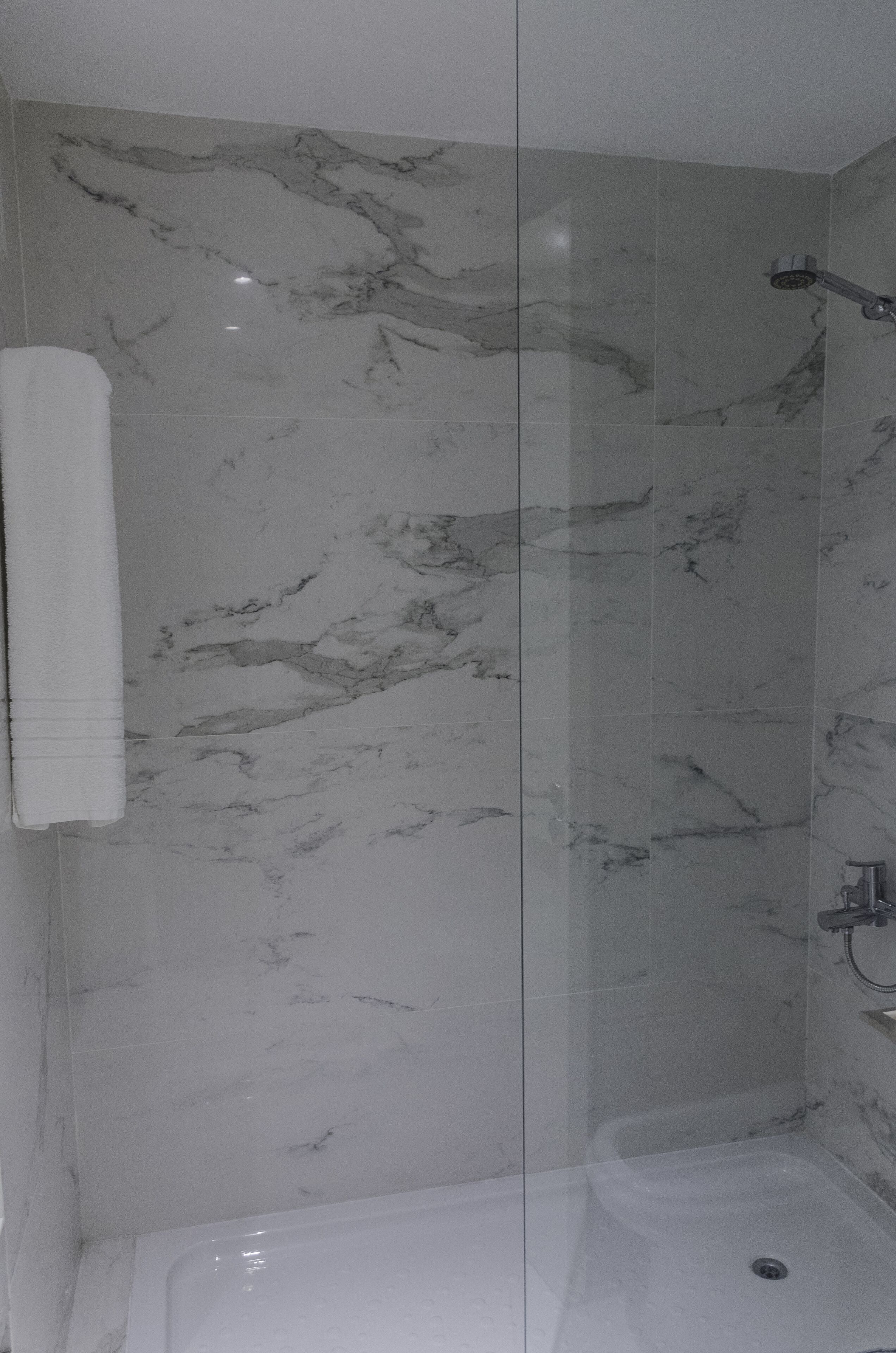 Un baño con paredes de mármol, cabina de ducha de vidrio y una bañera.