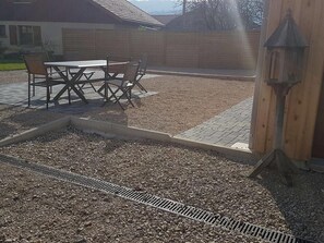 A patio area with a table and chairs, a wooden fence, and a gravel surface.