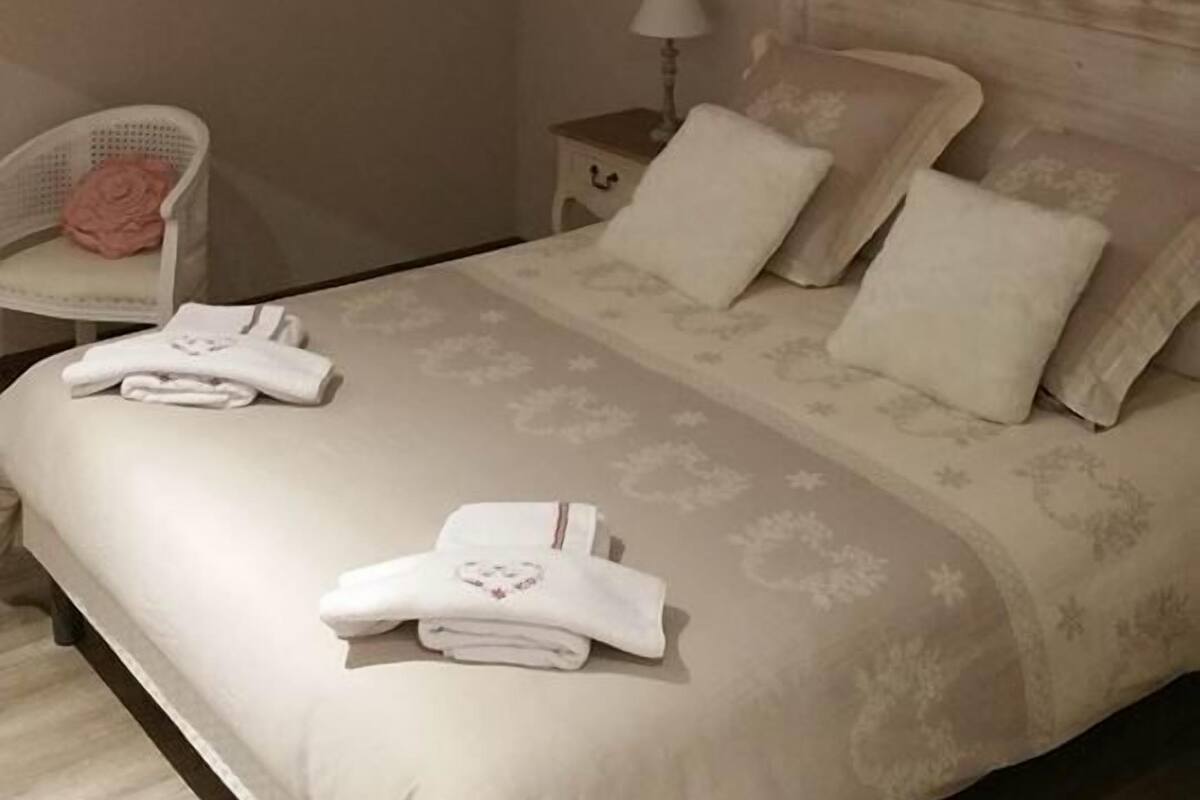 A bedroom with a sloped ceiling, a bed with white linens, a nightstand with a lamp, and a chair with a pink cushion.