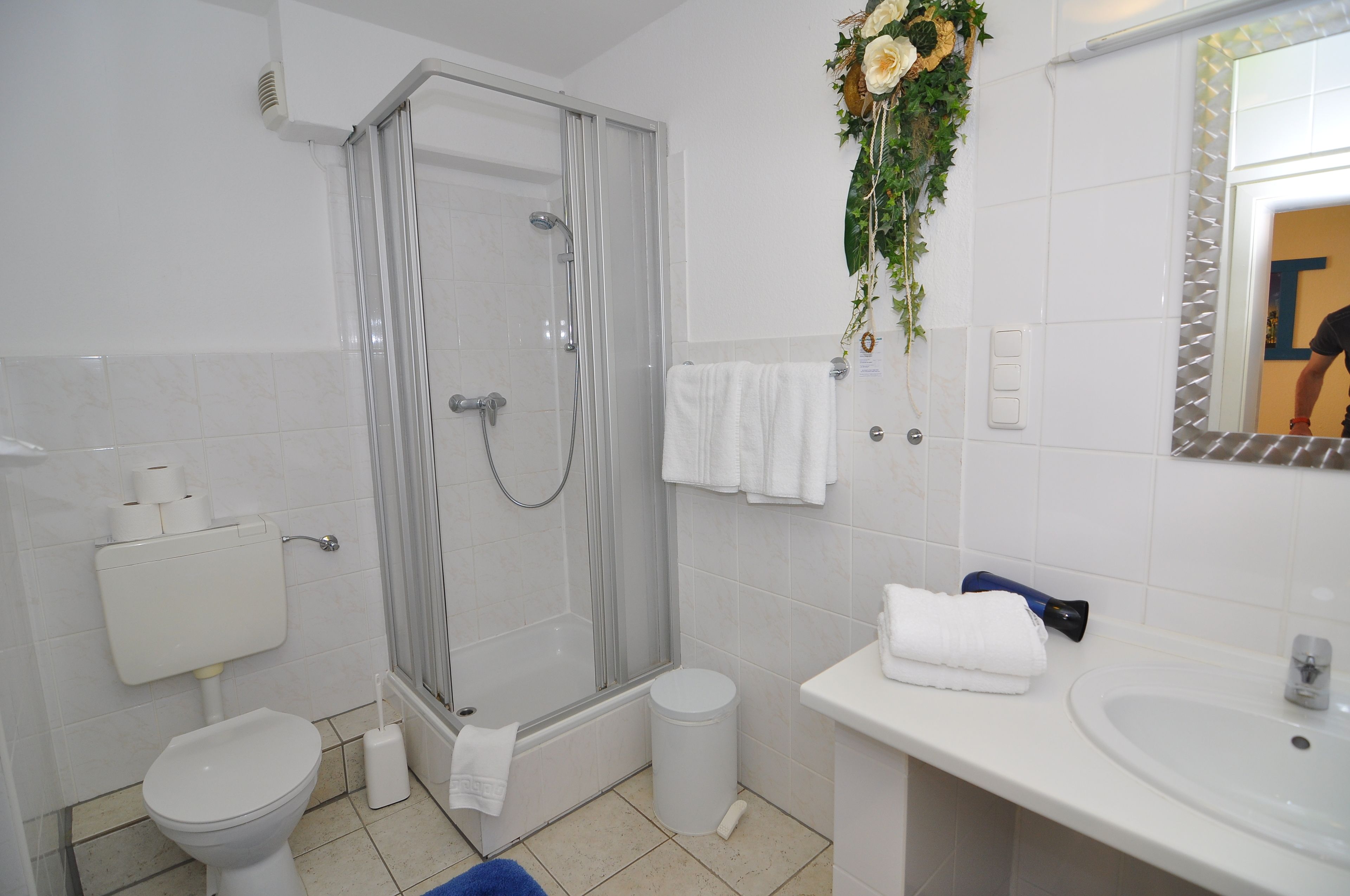 A bathroom with a toilet, shower, sink, and a mirror with a decorative plant.
