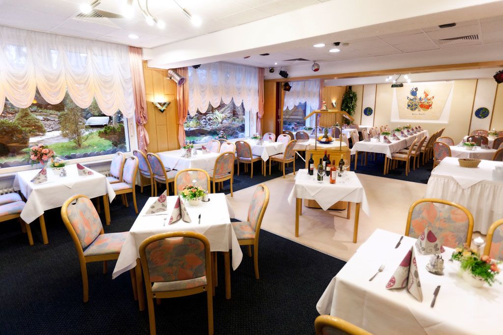 Un restaurante con varias mesas y sillas, decorado con manteles blancos y centros de mesa florales.