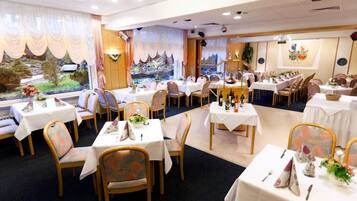 Un restaurante con varias mesas y sillas, decorado con manteles blancos y centros de mesa florales.