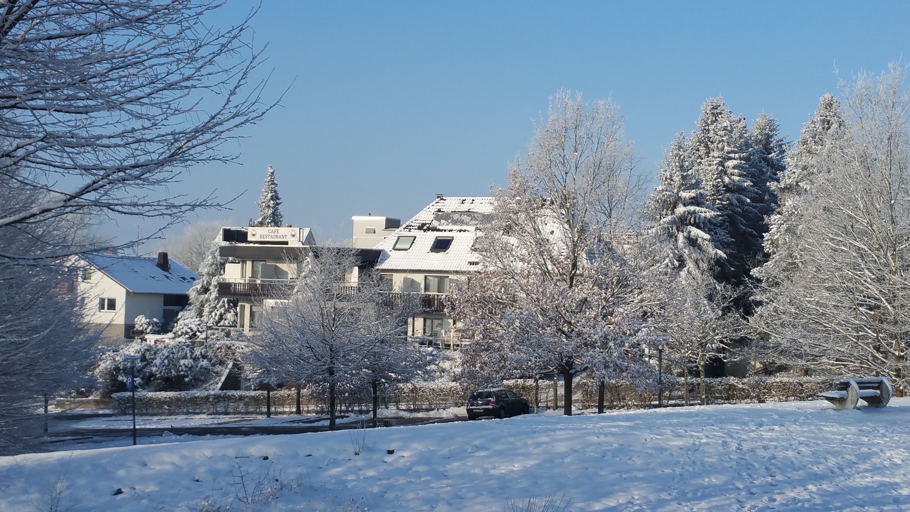 A snow-covered residential area with houses, a parked car, and a sign for a cafe restaurant.