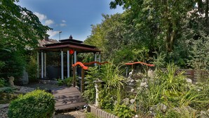 A garden with a wooden gazebo, stone pathway, and various plants. - Themenhotel Terrassen Café (Bad Muender am Deister)