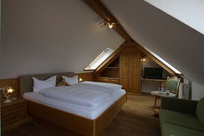 A bedroom with a wooden bed, a nightstand, a desk with a chair, and a television. - Hotel Jägerhaus (Sankt Peter)