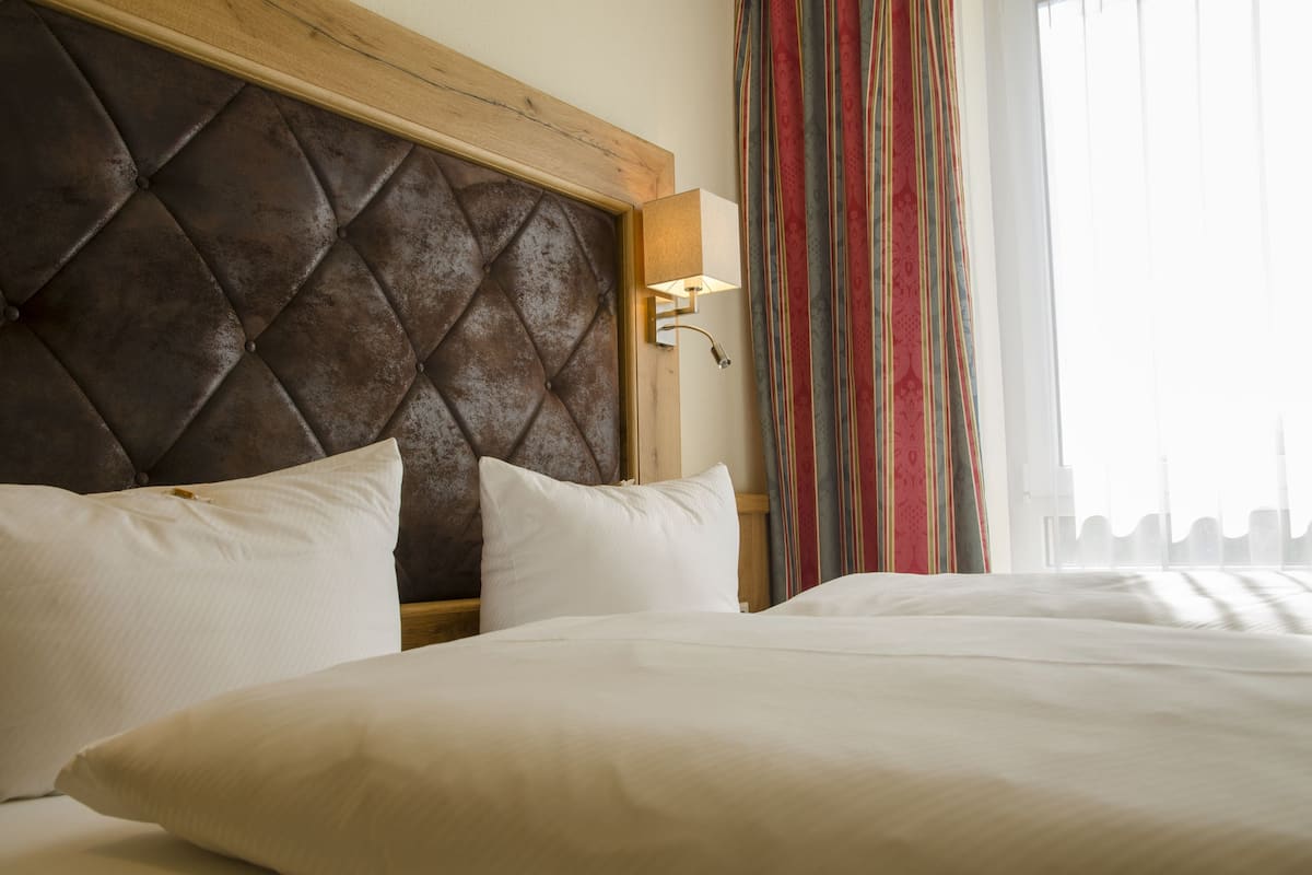 Habitación de hotel con cabecera capitonada, lámpara de noche y vista a una cortina a rayas.