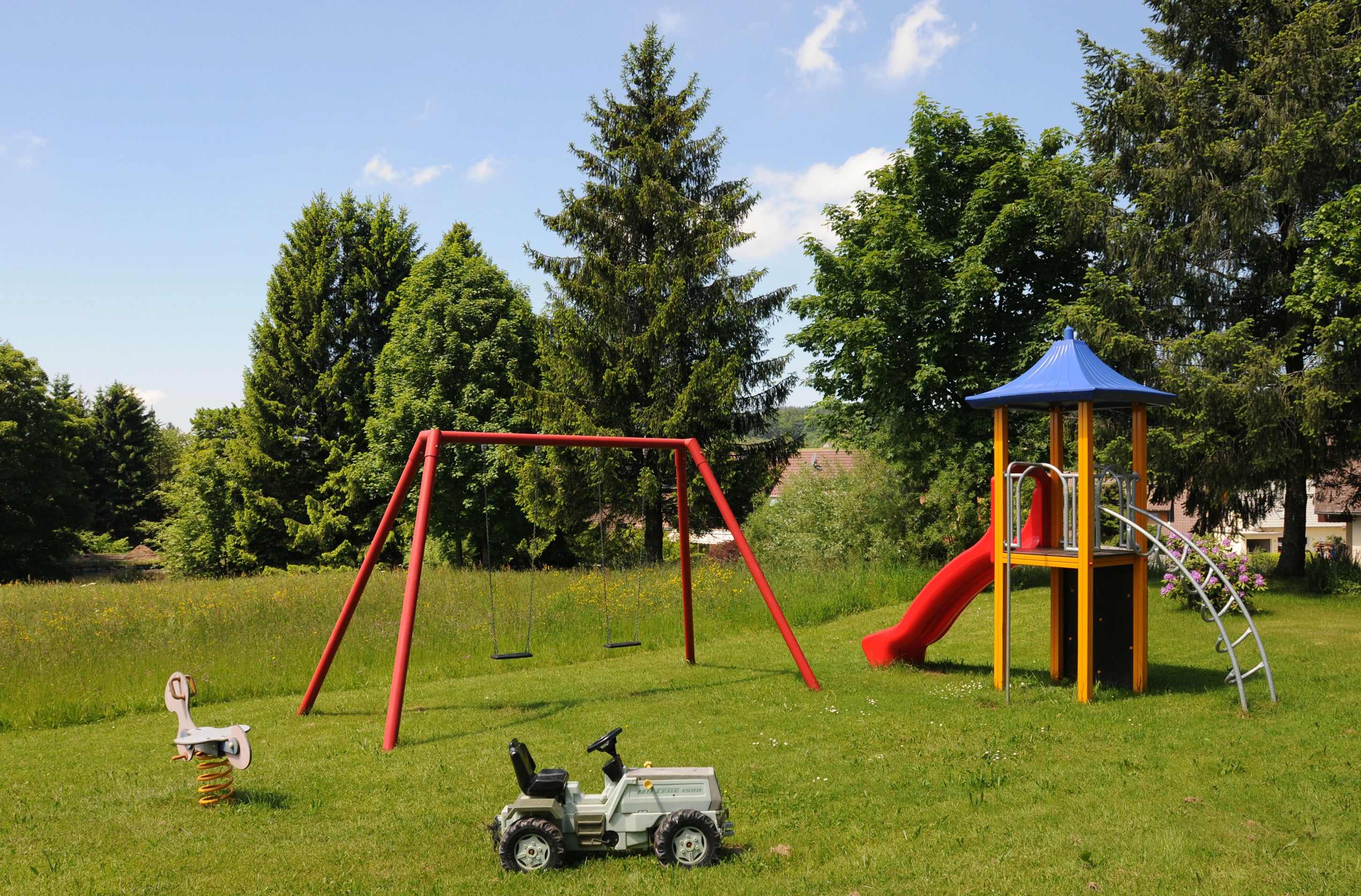 A playground with swings, a slide, and a small tractor toy.