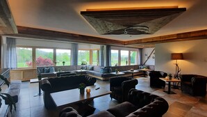 A spacious living room with a large window, a sofa set, a coffee table, and a fireplace. - Hotel Jägerhaus (Sankt Peter)