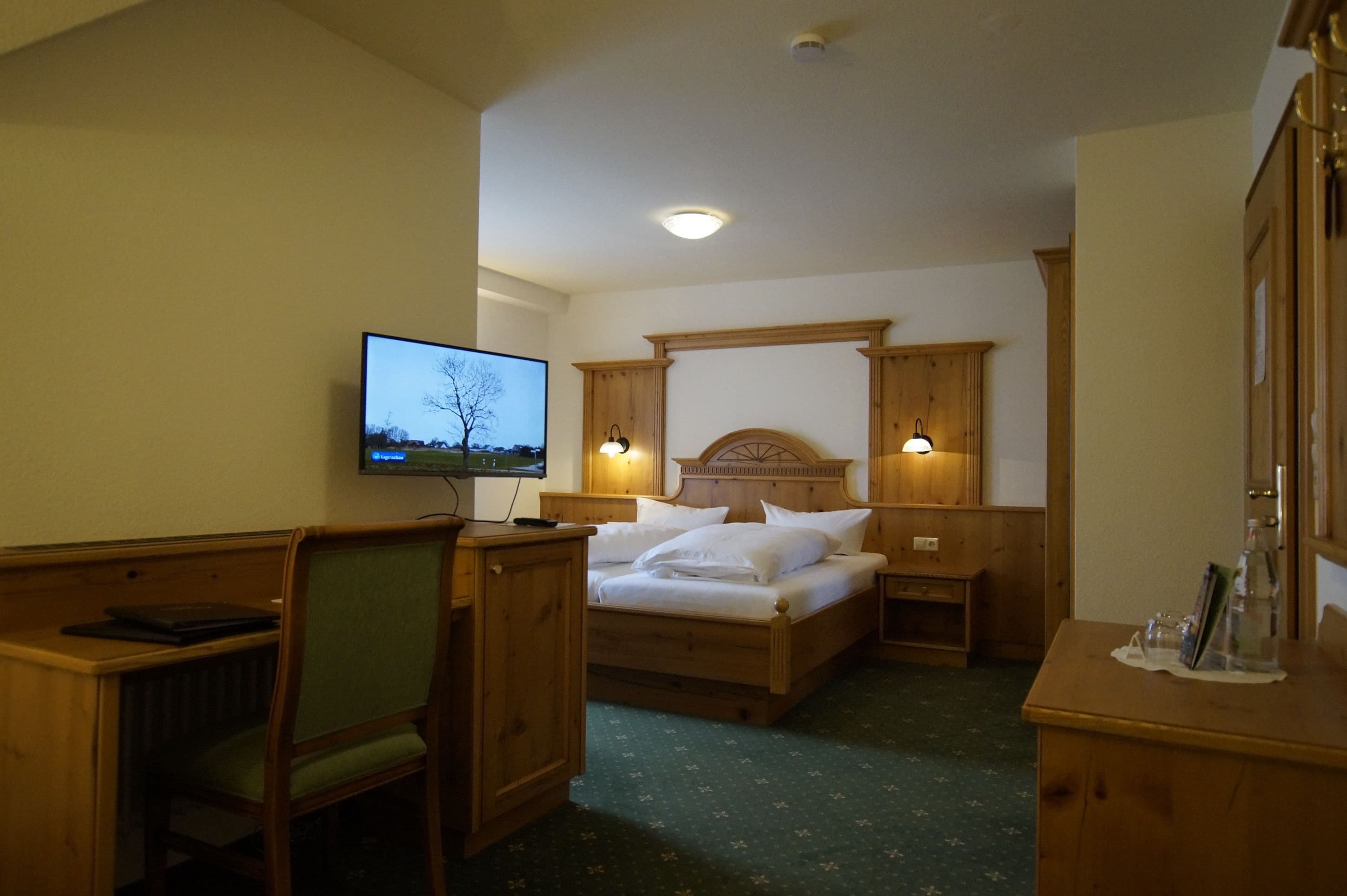 Ein Hotelzimmer mit einem hölzernen Bett, einem Schreibtisch mit Stuhl, einem Fernseher und einem Nachttisch mit Lampe.