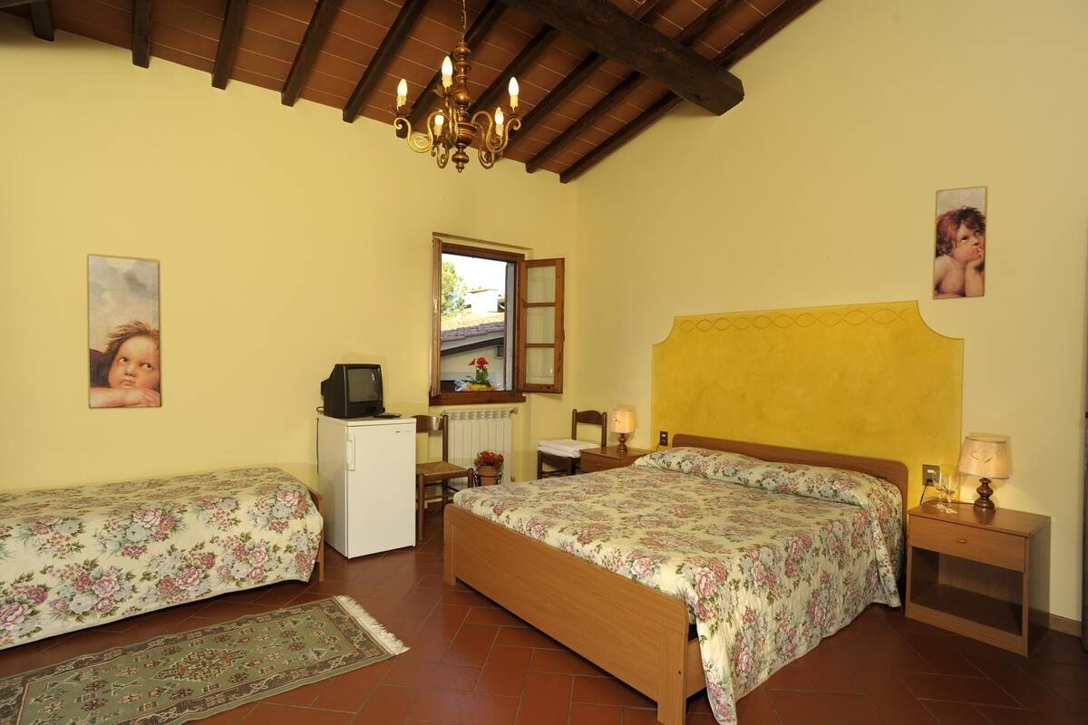 A bedroom with two single beds, a small desk with a television, a radiator, and a window with a view of the outside.