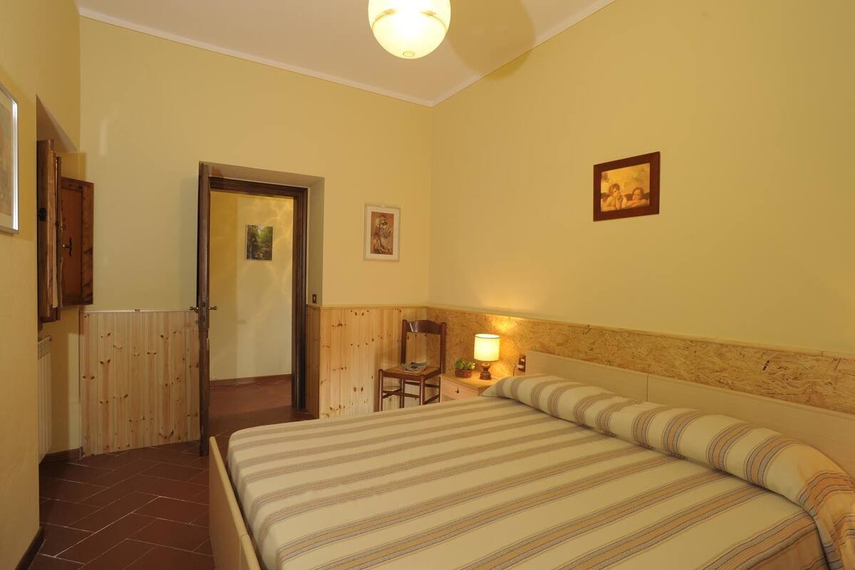 A hotel room with a bed, a chair, a nightstand, a lamp, and a door leading to another room.