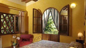 Ein Schlafzimmer mit einem großen Bett, Holzbalken, einem Fenster mit Vorhängen und einem Nachttisch mit Lampe.