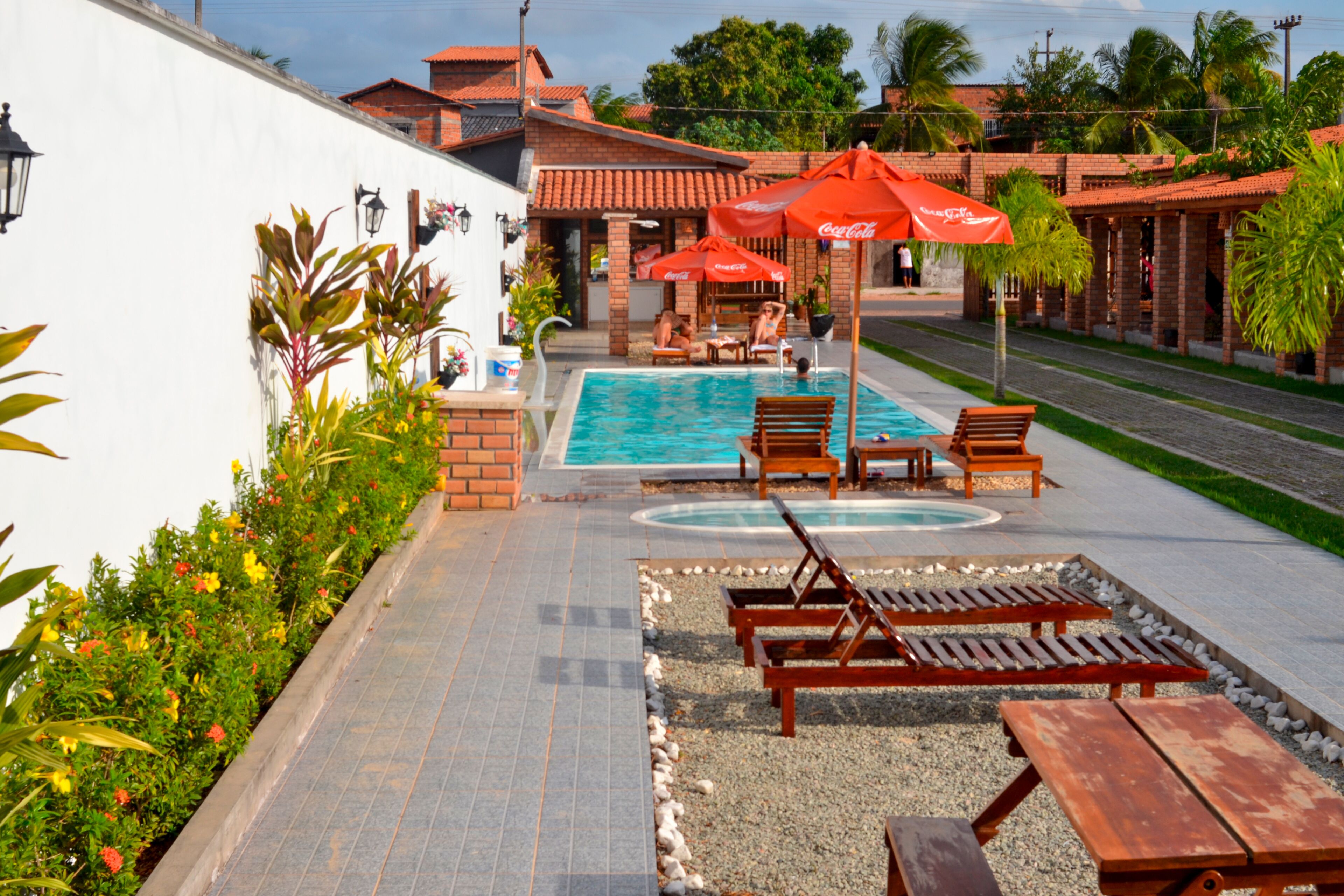 A pool area with lounge chairs and umbrellas, surrounded by a brick building and greenery.