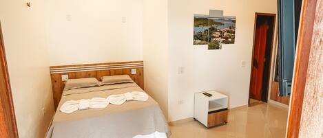 A bedroom with a bed, a bedside table, a small cabinet, a picture on the wall, and a door leading to another room.