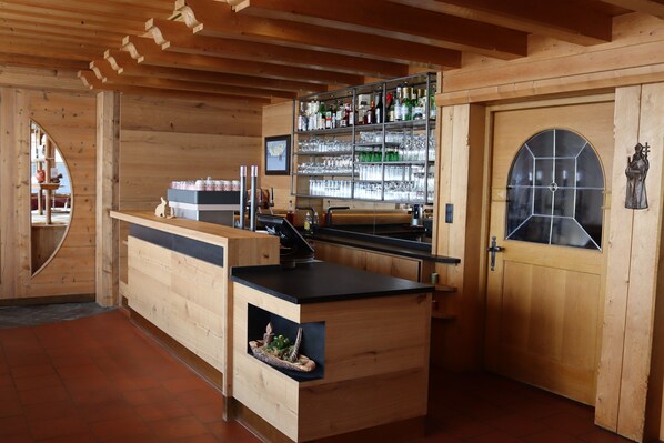 Un interior de madera con una zona de bar, estanterías llenas de botellas y una puerta con ventanal.