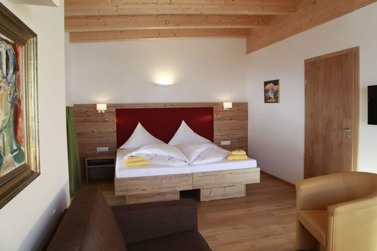 A bedroom with a wooden headboard, a bed with white linens, a brown sofa, and a wooden door.