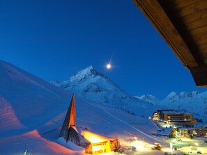 A snow-covered mountain with a lit building at its base, a clear sky, and a bright moon in the background. - Alpenhotel Seiler (Silz)