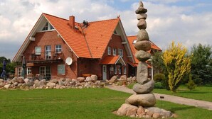 A large brick house with a red roof, a stone sculpture in front, and a well-maintained lawn. - Landhaus Bondzio (Langen Brütz)