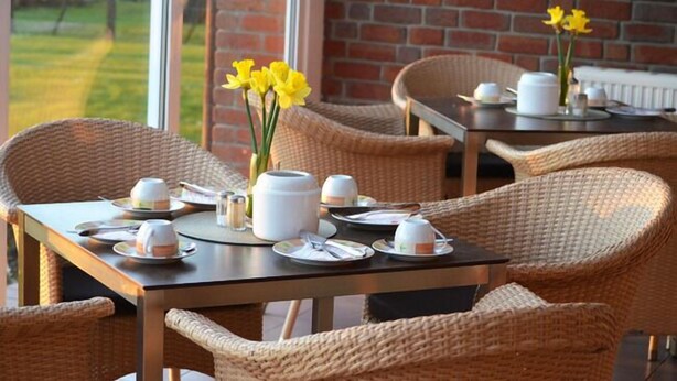 A dining area with wicker chairs and tables, each set with plates, cups, and a teapot. - Landhaus Bondzio (Langen Brütz)