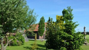 A building with a red roof, surrounded by lush green trees and a well-maintained lawn. - Landhaus Bondzio (Langen Brütz)