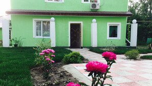 A green house with a tiled entrance and a small garden with pink flowers. - Alma Cinema Hostel (Almaty)