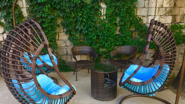A set of wicker chairs with blue cushions and a small round table in an outdoor setting. - Alma Cinema Hostel (Almaty)