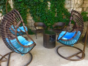 Un ensemble de chaises en osier avec des coussins bleus et une petite table ronde, le tout installé dans un espace extérieur.