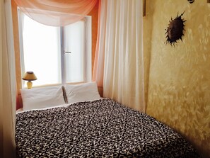 Une chambre à coucher avec un lit, des rideaux blancs, une fenêtre et un élément de décoration murale.