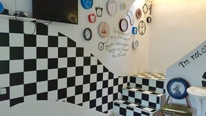 A staircase with a black and white checkered pattern, a wall decorated with various clocks, and a sign that says "I'm not cool." - Alma Cinema Hostel (Almaty)