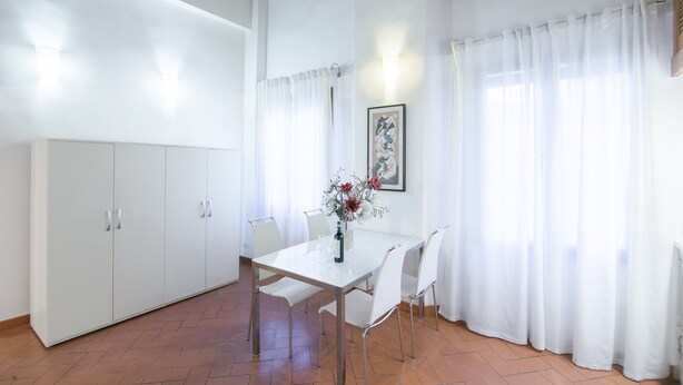 A dining area with a white table and chairs, a vase with flowers, and white curtains. - San Niccolò Loft by Mmega (Florence)