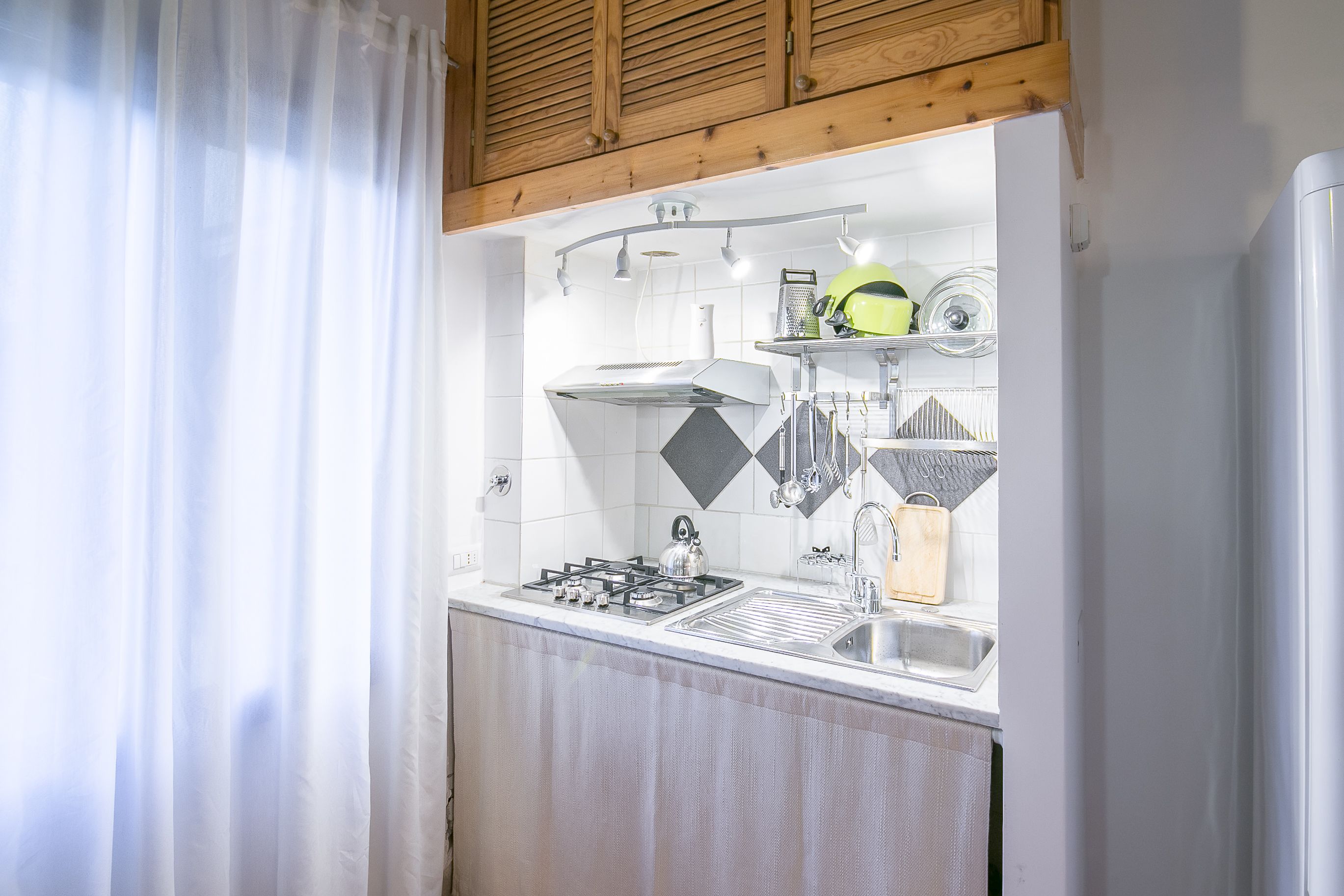 A kitchen with a gas stove, sink, and hanging utensils.