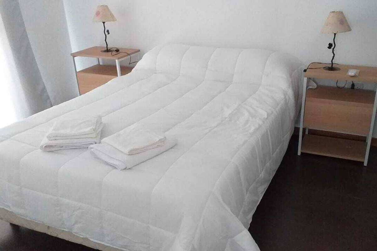 A neatly made bed with white linens and two bedside tables with lamps.
