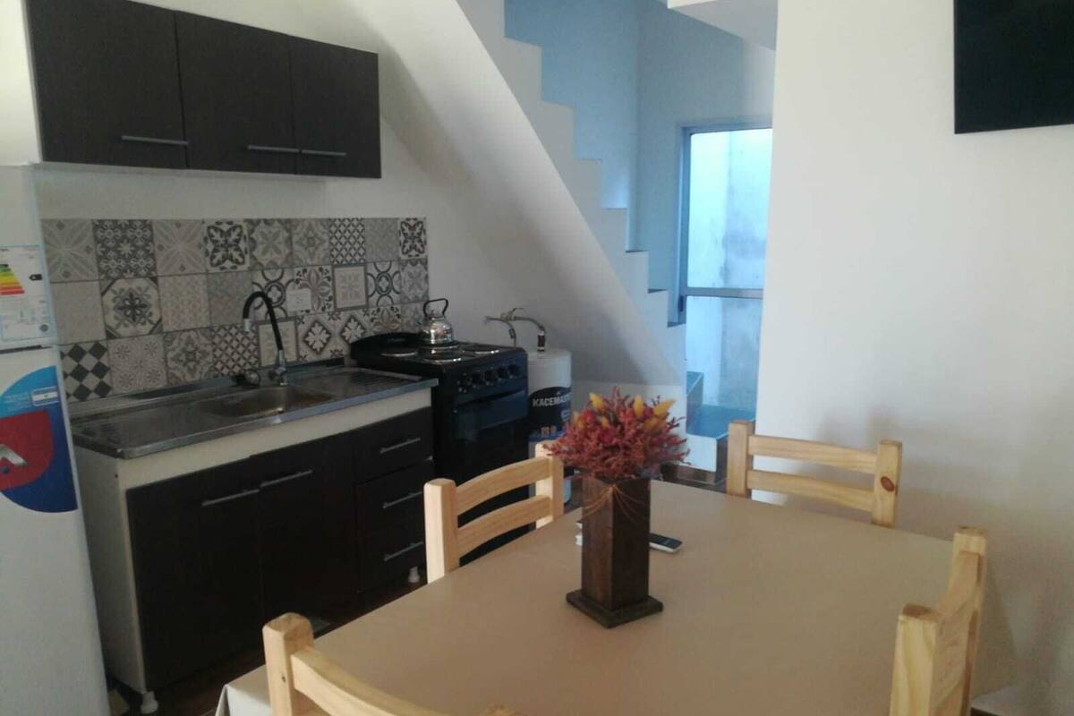 A kitchen with dark cabinets, a tiled backsplash, a stove, and a dining table with chairs.