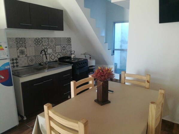 Una cocina con armarios oscuros, un protector contra salpicaduras de azulejos, una estufa y una mesa de comedor con sillas.