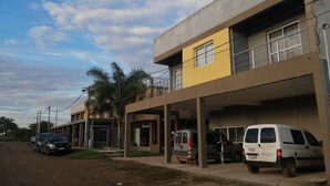 Un immeuble à plusieurs étages avec une façade jaune, un espace de stationnement et deux fourgonnettes blanches garées devant.