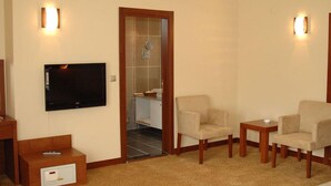 A living room with a flat-screen TV, a wooden cabinet, a remote control, and two beige armchairs. - Paluri Hotel (Hopa)